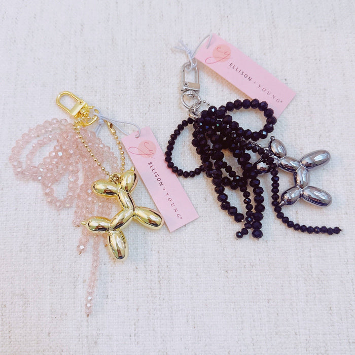 Ellison+Young balloon dog bag charm with beaded bow, featuring a playful design and detailed craftsmanship, attached to a handbag.