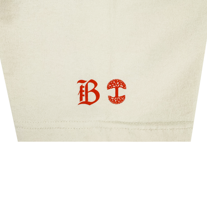 Close-up of heavy-weight cotton on the Bay FC Jubilee Tee: near the hem are two red symbols—a Gothic "B" on the left and a circular, tree-like emblem on the right.