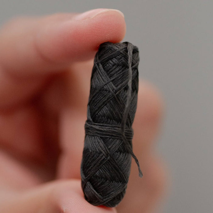 Hand holding spool of charcoal dental floss on gray background