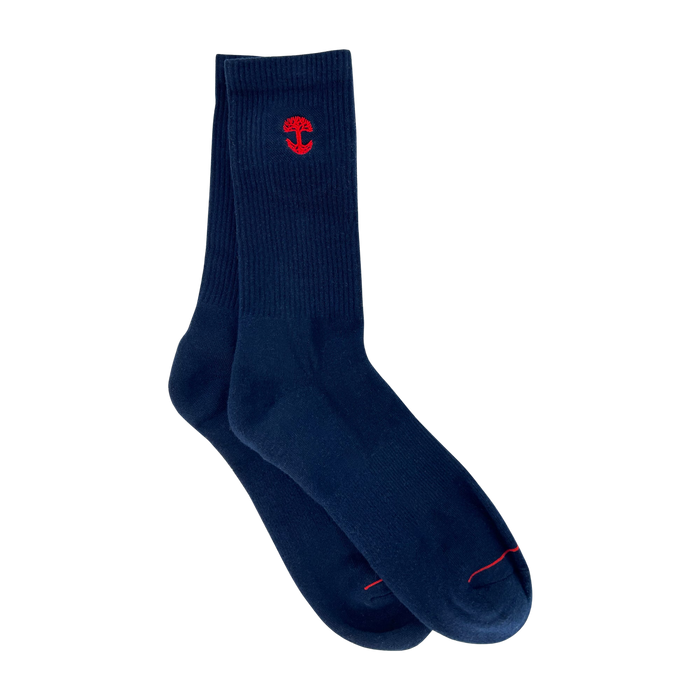 A pair of Embroidered Logo Socks from Oaklandish, in a deep navy blue color with a ribbed texture near the top. Each sock showcases a small red tree emblem, similar to the Oaklandish logo, near the cuff. The adult-size socks are slightly overlapped, with one sock's toe resting on the other's cuff, all set against a plain light grey background.