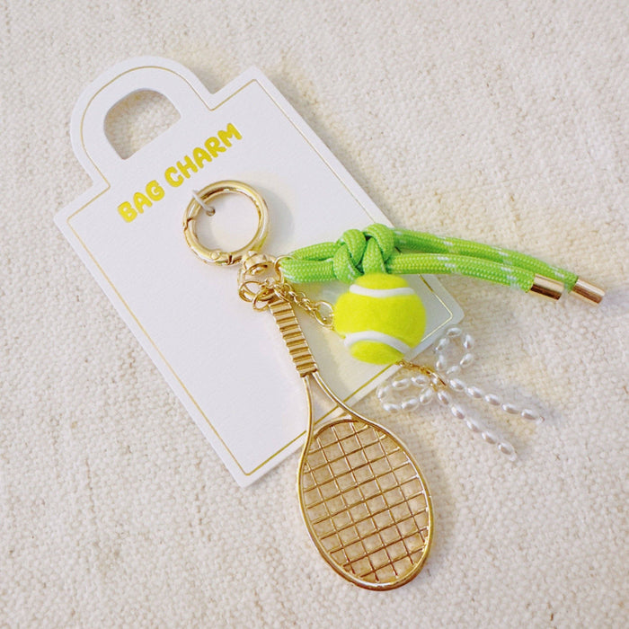 Ellison+Young Match Point tennis bag charm with sporty gold, neon accents, tennis racket and ribbon details on a keychain.