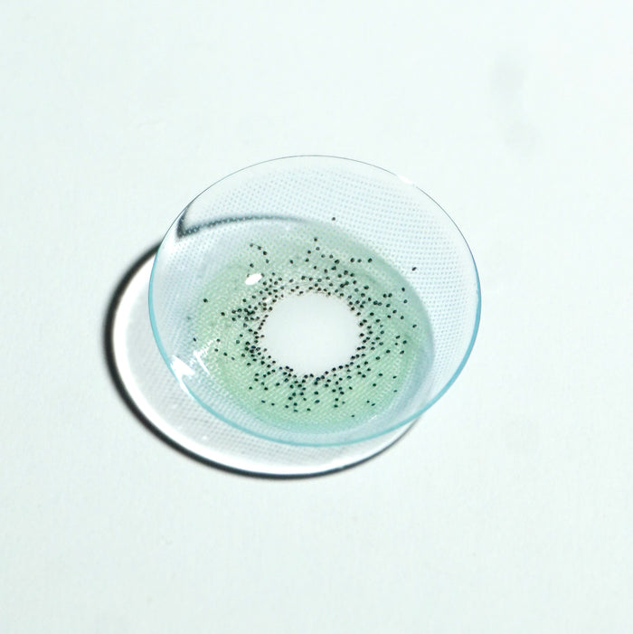 A close-up of the EyeCandys Pink Label Amalfi Blue contact lens, featuring a dotted pattern, is shown on a white surface, highlighting its vibrant blue color and unique design.