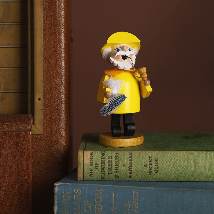 Wooden figurine of a character in a yellow raincoat and hat on top of books with a brown background