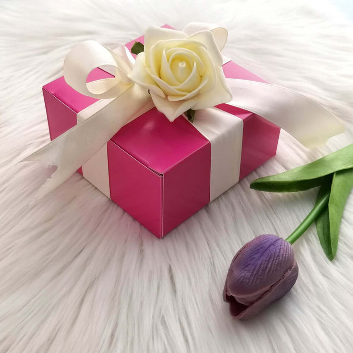 Pink gift box with a white ribbon and rose, accompanied by a purple tulip.