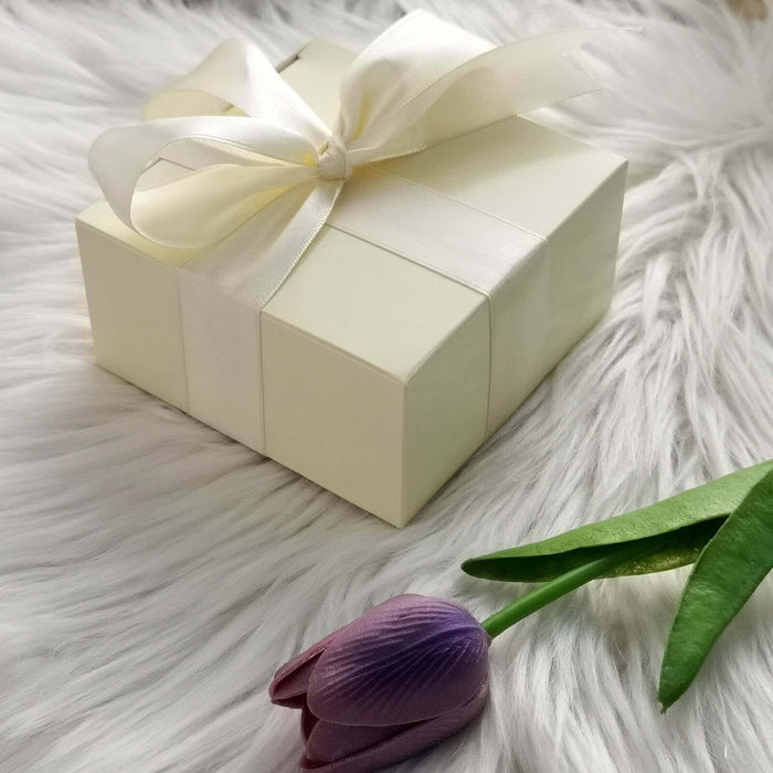 Elegant cream gift box with ribbon beside a purple tulip on soft fur.
