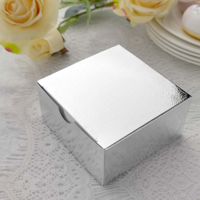Silver square gift box on a textured table with flowers in the background.