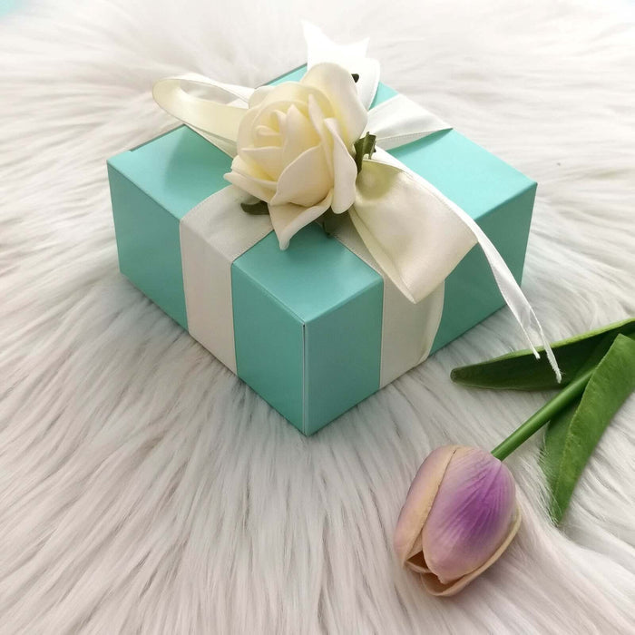 Turquoise gift box with white ribbon and flower decoration on a soft white surface.