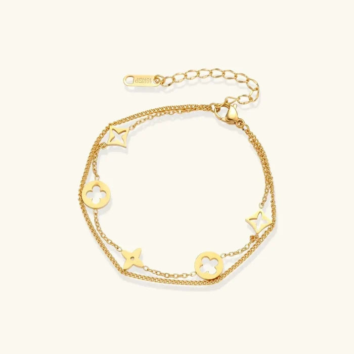 Double-layer gold-plated bracelet with quatrefoil and star charms on cream background, 18K gold finish.
