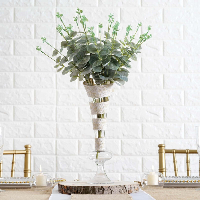 Decorative faux plant arrangement in a glass vase on a rustic table setting.