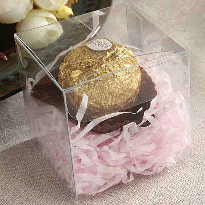 Clear gift box with gold chocolate ball and pink shredded paper inside.