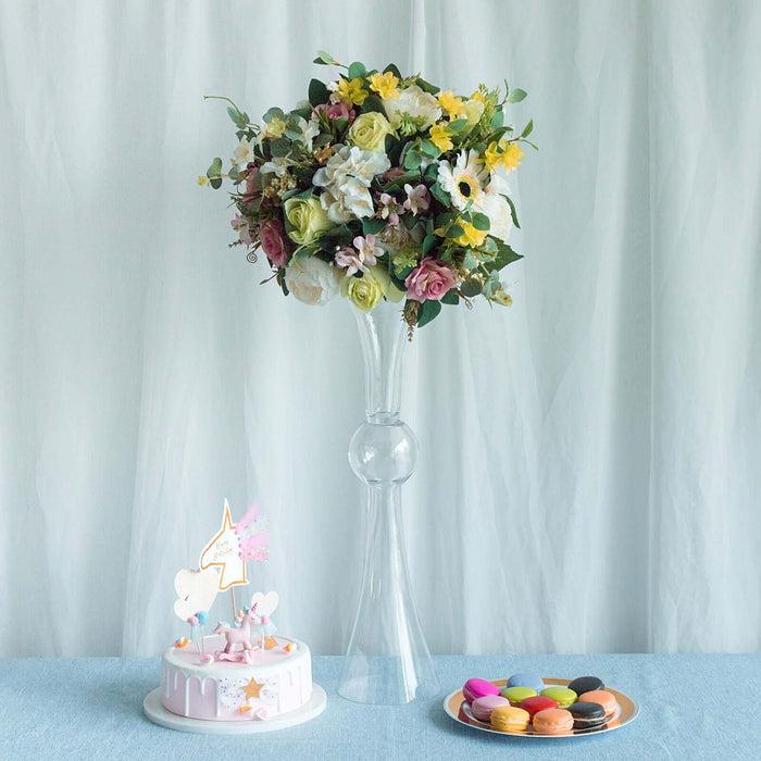 Floral arrangement in a tall vase with a cake and colorful macaroons on a table.