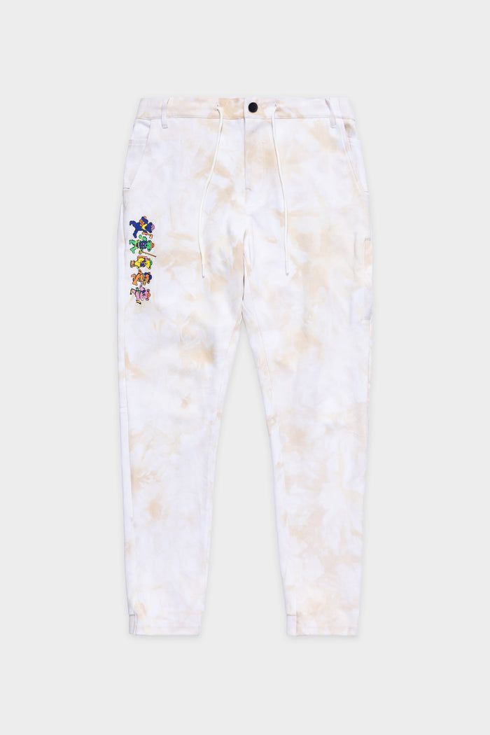 The 686 Mens Everywhere Double Knit Pant by 686 features a white tie-dye design, drawstring waist, button closure, and small, colorful cartoon character graphics arranged vertically on the left thigh.