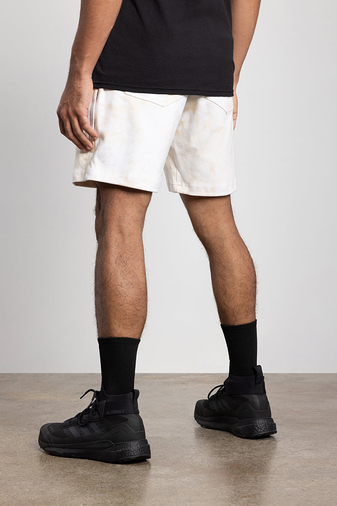A person stands on a concrete floor, shown from the waist down, wearing a black shirt, 686 Mens Everywhere Double Knit Short by 686 in a light color, black crew socks, and black sneakers against a plain light background.