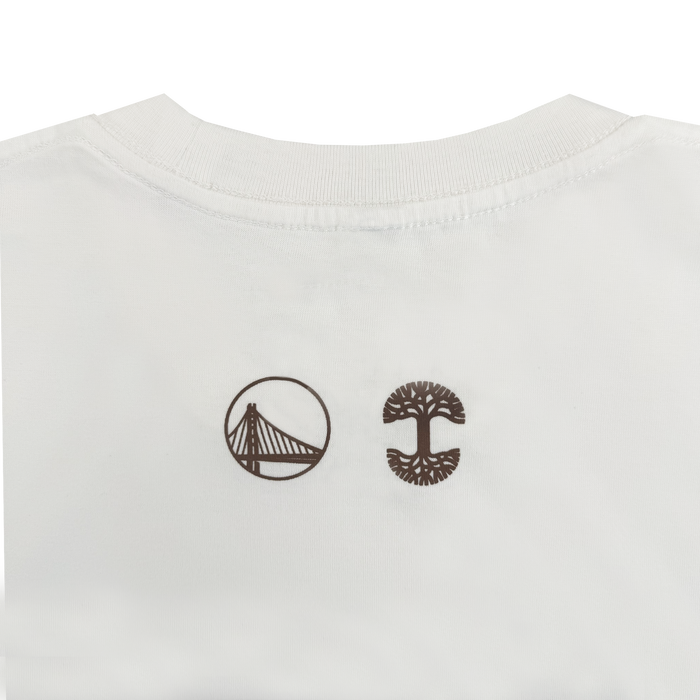 White fabric tee from Other’s 70's Trading Card collection featuring two brown logos: a stylized suspension bridge in a circle on the left, inspired by classic Warriors x Oaklandish Town Collection motifs, and a tree with detailed canopy and visible roots reminiscent of the Timberland logo on the right. Both designs are printed near the neckline, subtly referencing traditional Warriors jersey details.