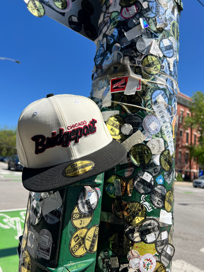 Cap with 'Chicago Bridgeport' on a pole covered in stickers on a street.