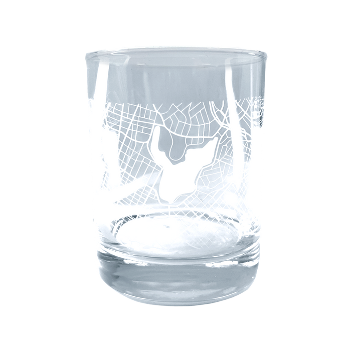 Introducing the Oaklandish Aerial Tumbler, a clear whiskey glass adorned with an intricate etched design that mirrors an aerial map of Oakland. Featuring distinctive lines and a central shape that could indicate a lake or landmark, this classic tumbler boasts a thick base and smooth, cylindrical contour.