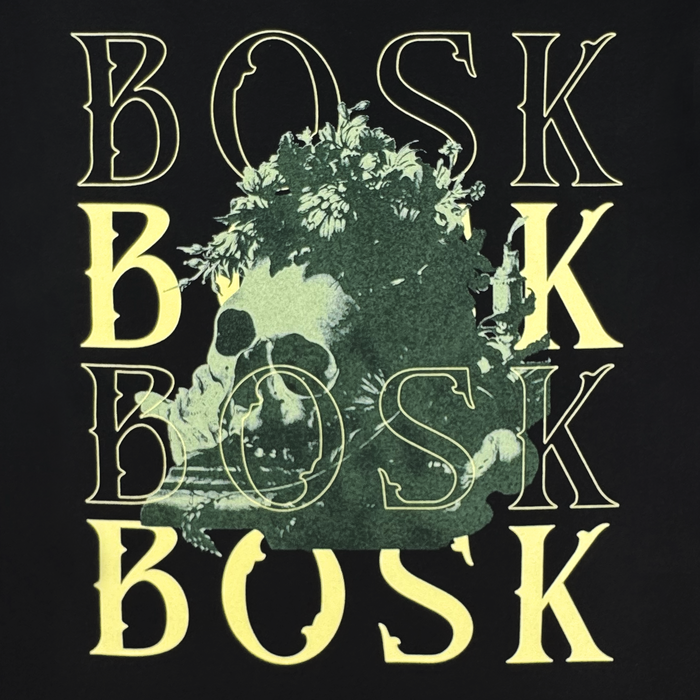 The image showcases the word “BOSK” repeated four times in bold yellow lettering, with a human skull partially obscured by green leaves and foliage at its center. These elements overlap against a deep black backdrop, creating a striking design featured on the Allure LS Tee by Other—a classic fit long sleeve t-shirt made from heavyweight cotton.