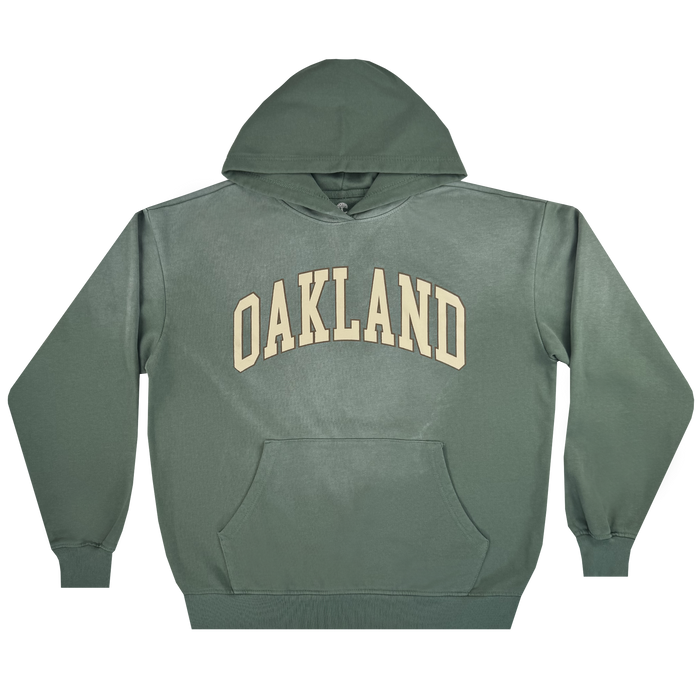 The Oaklandish Alma Mater Hoodie 2.0 is a men's green pullover, made from 100% cotton with a large front pocket and bold cream “OAKLAND” lettering across the chest, shown laid flat on a white background.