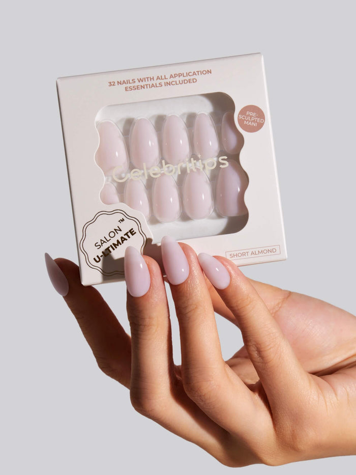 A hand wearing Salon-Ultimate pink short almond nails holding a box of the nails on a white background.