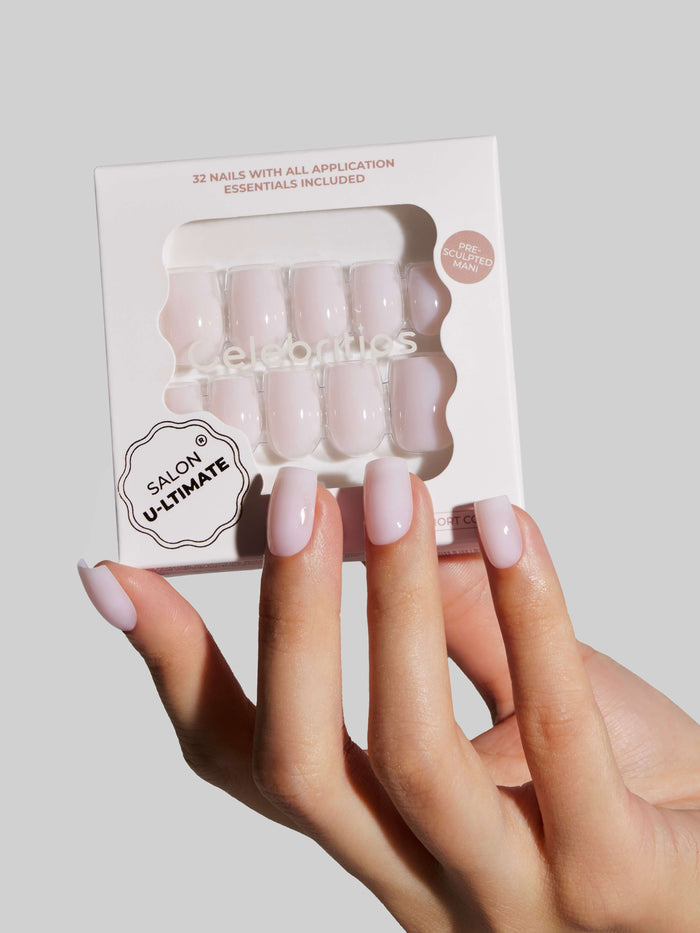 Hand holding a package of beige press-on nails with a neutral background