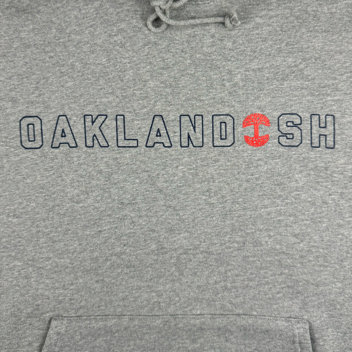 The Bandit Hoodie by Oaklandish is a heather grey pullover featuring "OAKLANDISH" in black letters across the chest, with a red tree ring design replacing the "I". Crafted from soft fabric, it includes drawstrings on the hood for a casual feel. Available in men's sizing for an ideal fit.