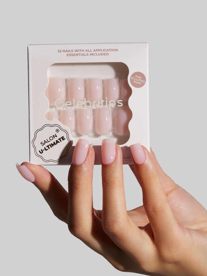 Hand holding a box of press-on nails with a neutral background