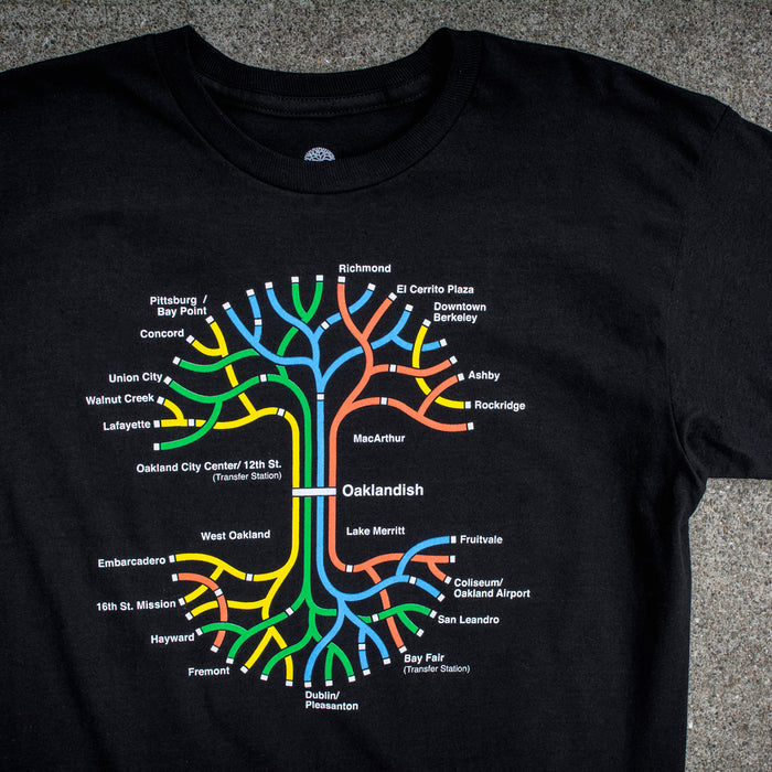 The BART Tree Tee by Oaklandish is a 100% cotton, classic fit t-shirt that features a vibrant map of the Bay Area Rapid Transit (BART) system. The design showcases various station names and lines in red, blue, yellow, orange, and green, all branching out from a central point labeled "Oaklandish," beautifully centered on the shirt.