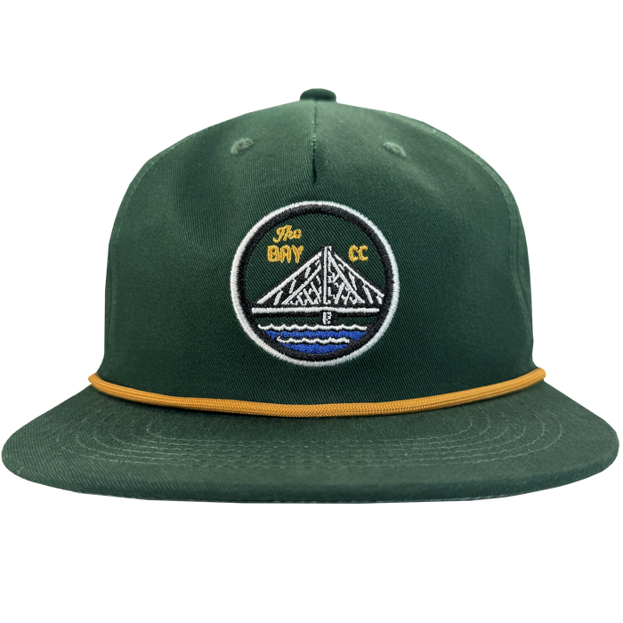The Bay Area 5 Panel by DOC from Oaklandish is a green hat with a structured crown, gold rope detail, and a patch showing a white bridge over blue water with "The Bay CC" in yellow on black.