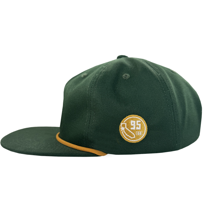 The Bay Area 5 Panel by DOC from Oaklandish is a dark green hat with a flat brim and yellow accent, side view. A circular patch displays a yellow banana and "95" in white, while small stitched eyelets adorn the crown.