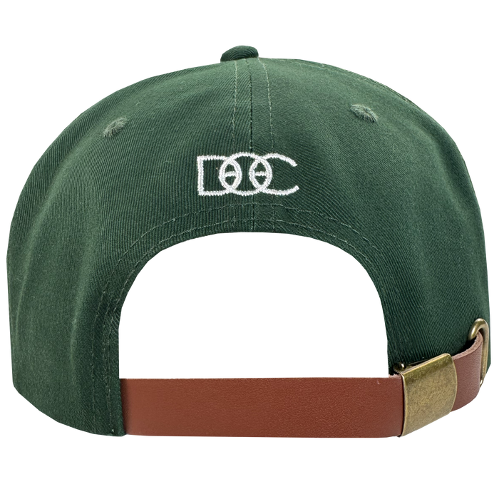 The Bay Area 5 Panel by DOC from Oaklandish is a green hat with "DOC" and two interlocking rings embroidered in white on the back. It features a brown adjustable strap with brass buckle. Displayed on a plain white background.