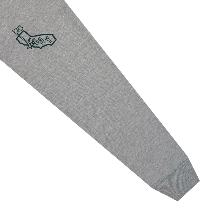 A gray heavyweight fleece sleeve from the Bay Area CC Hoodie By DOC includes a small outline of California near the wrist, with “BAY” and a waving flag graphic on the upper left to represent the San Francisco Bay Area. The ribbed cuff at the end of this cozy pullover hoodie sleeve is clearly visible.
