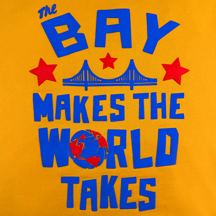 Yellow background with bold blue text: “The BAY MAKES THE WORLD TAKES,” flanked by two red stars on each side of a stylized bridge, with the letter “O” in “WORLD” illustrated as a globe. The Bay Bridge Hoodie by DOC from Other is inspired by the creative spirit of the Bay Area and captures the vibrant energy of an art project.