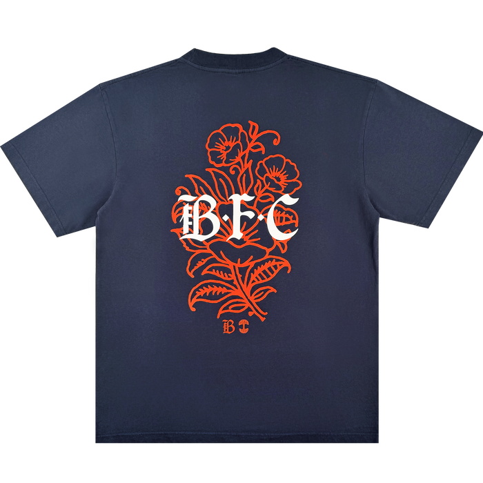 The Bay FC Flora Tee by Bay FC is a navy blue, classic fit shirt made from heavy-weight cotton. The back displays a large orange floral design with bold white "BFC" lettering and a small "BFC" below, celebrating Bay FC style.