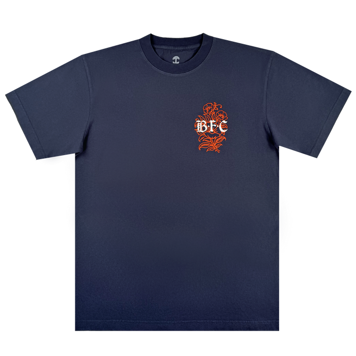 The Bay FC Flora Tee by Bay FC is a navy classic fit heavyweight cotton t-shirt featuring a small orange floral design and white "BFC" text on the left chest, laid flat on a plain white background.