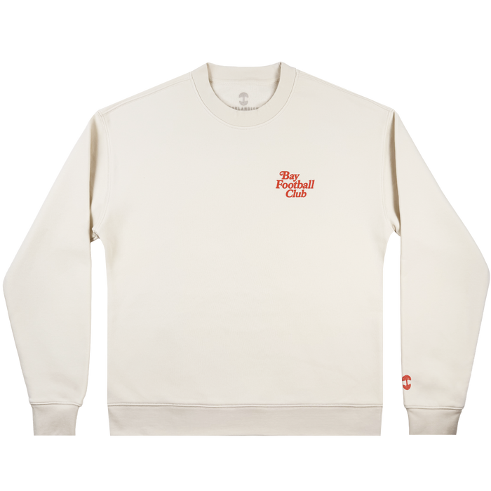 The Bay FC Jubilee Crew is a cream crewneck sweatshirt with "Bay Football Club" in small red text on the left chest and a red logo on the left sleeve cuff. Shown in men's sizing, it’s laid flat on a white background.