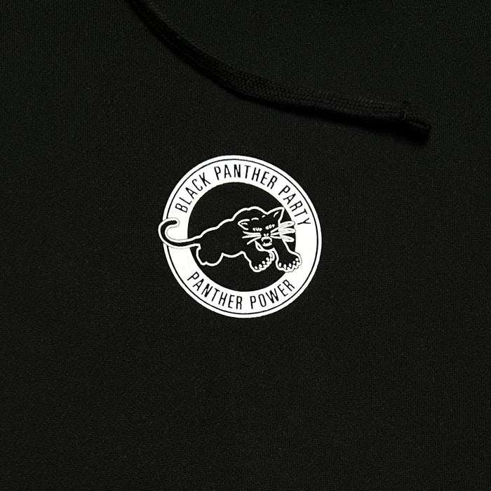 Close-up of the Black Panther Power Hoodie by Oaklandish. This black pullover hoodie features a circular logo in white, displaying an illustration of a black panther ready to pounce. The text "Black Panther Party" arches over the panther, while "Black Panther Power" is inscribed below. The logo is centrally positioned on the hoodie.