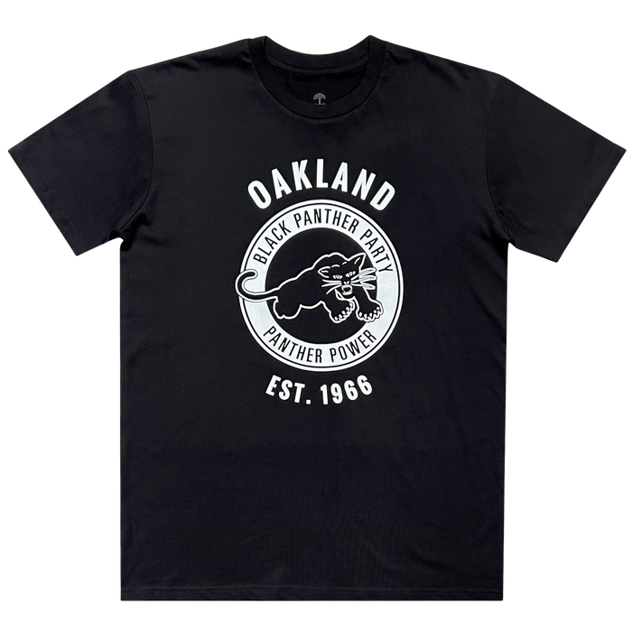 The Black Panther Power Tee by Oaklandish is a black T-shirt showcasing a white circular logo at the center. Inside the circle, it features an image of a black panther along with the phrases "Oakland Black Panther Party" and "Black Panther Power." The text "Oakland" is displayed above the circle, while "Est. 1966" is boldly written below—all in striking white text. This piece from Social Consciousness Apparel comes with short sleeves.