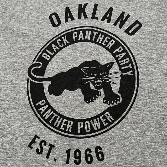 The Black Panther Power Tee by Oaklandish features a black design on a gray t-shirt with a central image of a panther in a pouncing position. The text "BLACK PANTHER PARTY" encircles the top of the panther, while "PANTHER POWER" is at the bottom. Above and below this circular design, additional text celebrates the influential community organization with "OAKLAND" and "EST. 1966.