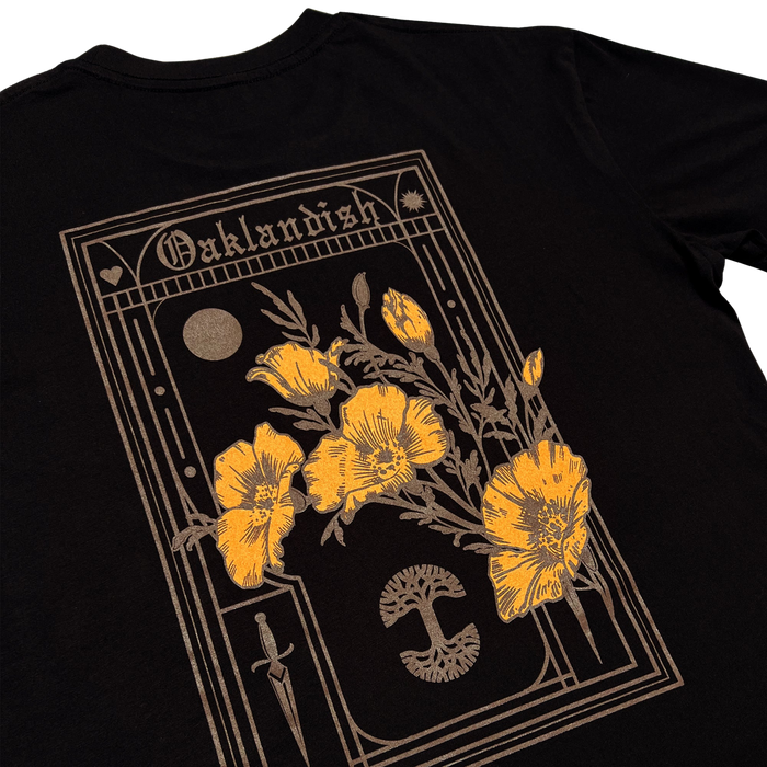 Oaklandish's Blossom Tee is a black men's cotton t-shirt with an intricate design. The design features a large rectangle at the top with the word "Oaklandish", a moon, a heart, and a dagger. Inside the rectangle are several yellow poppy flowers—the California state flower—displayed with detailed stems and leaves over a black mushroom graphic.