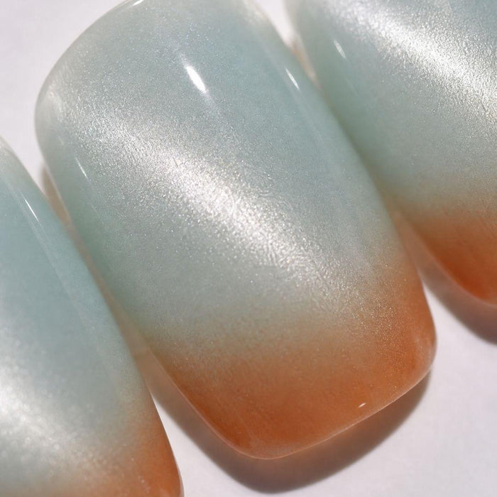 Close-up of EyeCandys Blue Hour Latte Press-On Nails—three handmade nails feature a smooth, glossy gradient from shimmery light blue tips to warm peach bases, perfectly mimicking a salon-quality gel manicure.