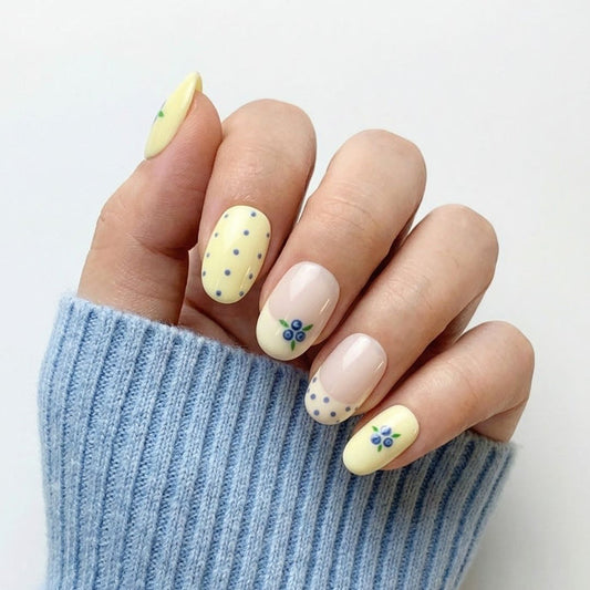 Hand wearing EyeCandys Blueberry Tart press on nails featuring cream and blush base with blueberry clusters, green leaves, and blue polka dots.