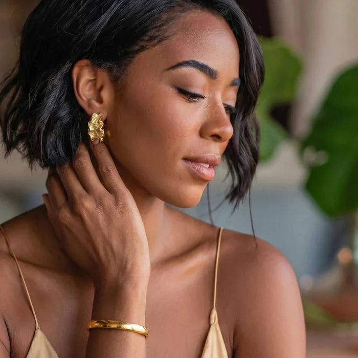 Bold Hinge Bangle in polished gold-tone metal, a slim rounded bracelet worn with a textured gold earring.