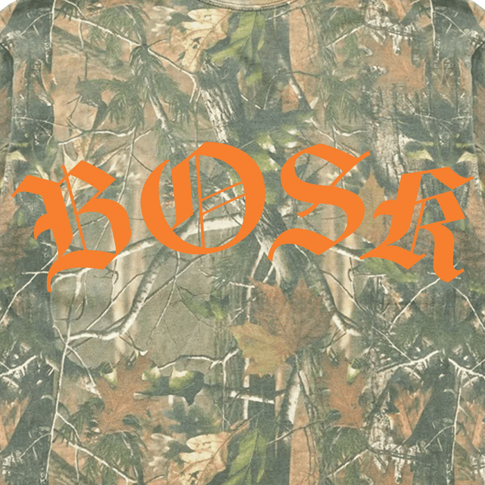 The BOSK Camo Tee by Other features a classic tree camouflage pattern with leaves, branches, and natural forest colors in green, brown, and tan tones. Bold orange Gothic-style lettering spelling “BOSK” stands out across the center, all printed on a heavyweight cotton oversized fit t-shirt.
