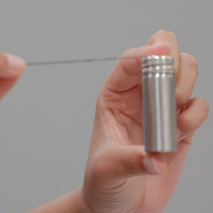 Hand pulling strand of charcoal dental floss from stainless steel container on gray background