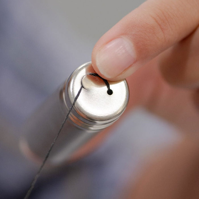 Hand pulling strand of charcoal dental floss from stainless steel container on gray background