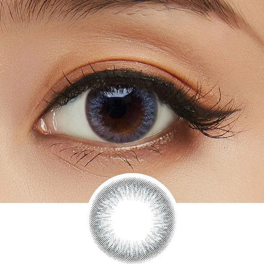 Close-up shot of model's eye adorned with Clalen Iris Blue Moon (30pk) daily color contact lenses with prescription, paired with clean-girl eye makeup, showing the brightening and enlarging effect of the circle contact lens on dark brown eyes, above a cutout of the contact lens with limbal ring on a white background.