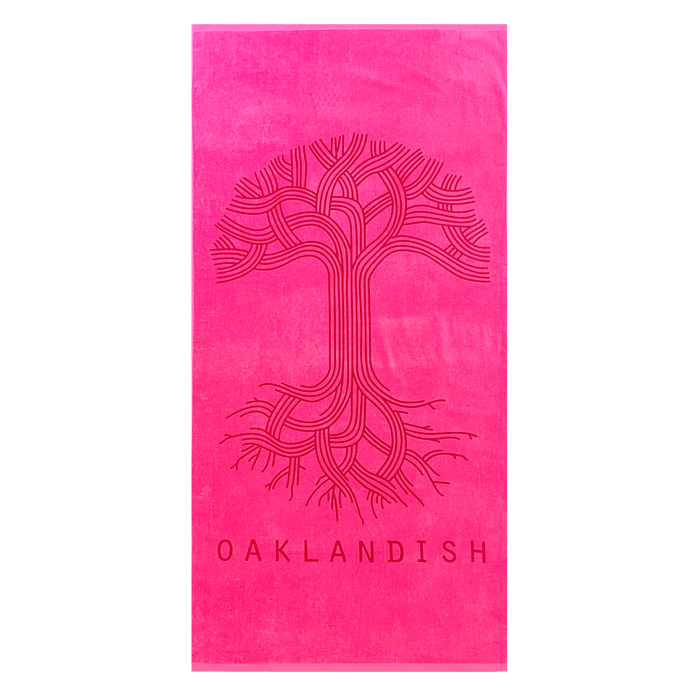 The Classic Logo Beach Towel by Oaklandish is a vibrant, oversized bright pink towel made from 100% ringspun cotton. It features an intricate, stylized tree design with intertwining branches and roots in the center. Below the tree, "OAKLANDISH" is printed in bold font, adding to its luxury and eye-catching appearance.