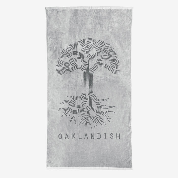 The Classic Logo Beach Towel by Oaklandish is a grey, oversized towel featuring an intricate, stylized tree design with numerous curved branches and roots in the center. Below the tree, "OAKLANDISH" is prominently displayed in capital letters. Made from 100% ringspun cotton, this super soft towel features a lighter grey background.