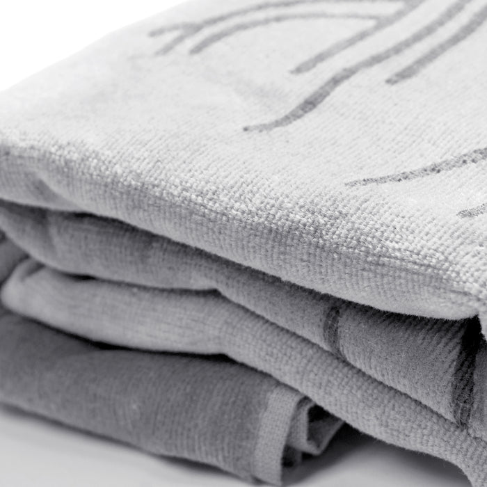 A neatly arranged stack of three folded Classic Logo Beach Towels in various shades of gray rests on a smooth, white surface. Made from 100% ringspun cotton, these Oaklandish towels feature a textured surface with faint abstract patterns. The top towel showcases a subtle curved design, while the others are more plain and simple.