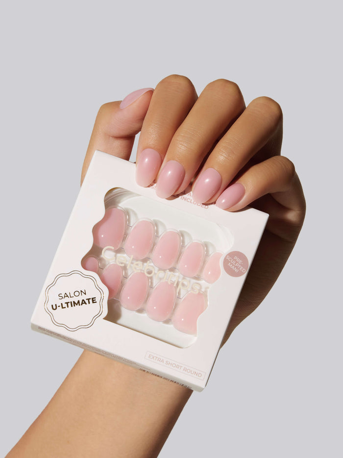 A hand holding Salon U-ltimate pink press-on nails on a white background.